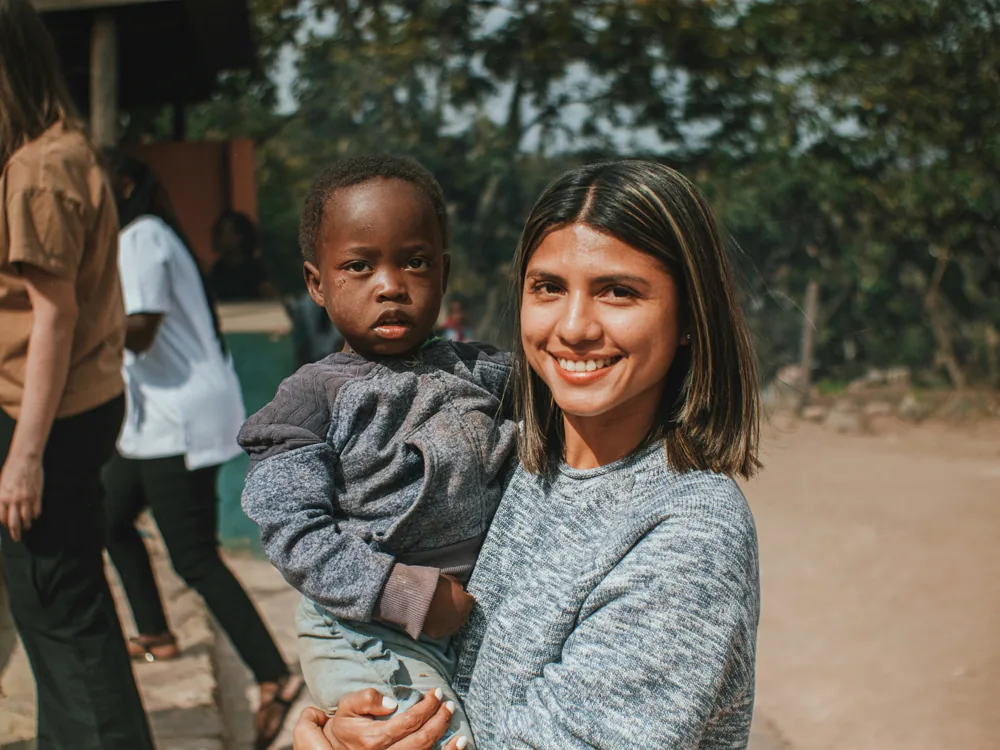 A woman smiling warmly as she holds a young child.