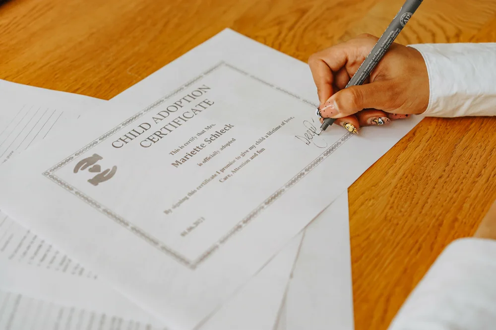 A hand signing a child adoption certificate.